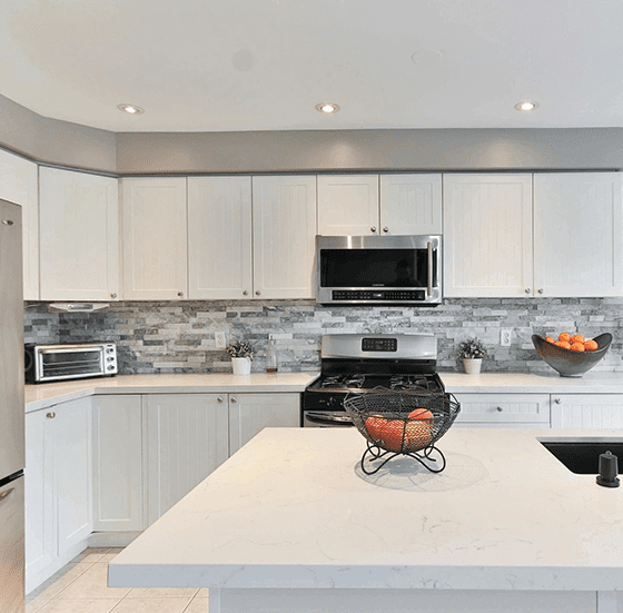 A kitchen with white cabinets and a bowl of fruit on the counter.