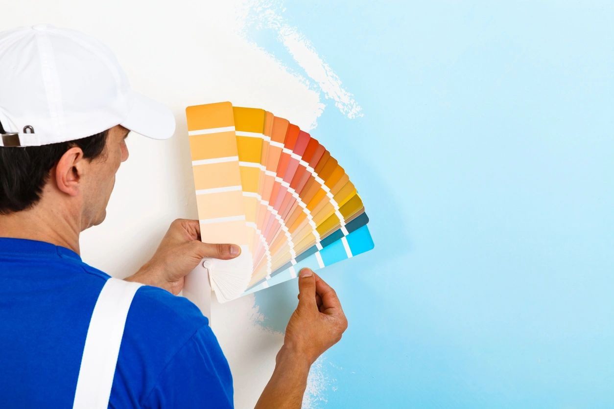 A person holding paint swatches in front of a wall.