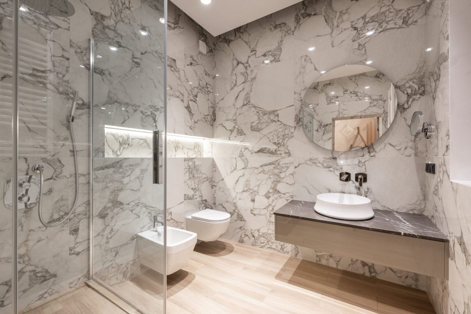 A bathroom with marble walls and floors, and a glass shower door.